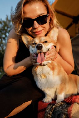 Galli Corgi Pembroke köpeği olan mutlu genç bir kadın yaz günü glamping yaparken dinleniyor. Açık hava eğlencesi ve dinlenme için lüks kamp çadırı. Yaşam tarzı kavramı