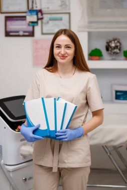 Farklı krem bankaları ve güzellik enjeksiyonlarıyla gülümseyen kadın kozmetik uzmanı. Kadın güzellik uzmanı kozmetoloji kliniğinde çalışıyor. 