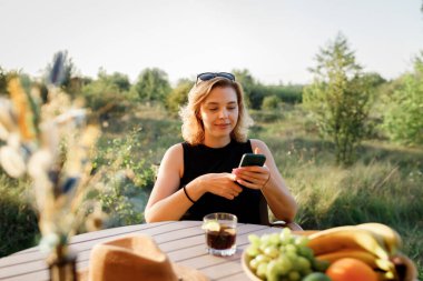 Mutlu Kadın Serbest Çalışan, güneşli bir günde rahat bir glamping çadırında dinlenirken telefonla içki içiyor. Yaz tatili ve tatil için lüks kamp çadırı. Yaşam tarzı kavramı