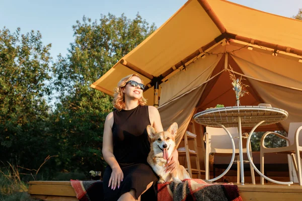 Galli Corgi Pembroke köpeği olan mutlu genç bir kadın yaz günü glamping yaparken dinleniyor. Açık hava eğlencesi ve dinlenme için lüks kamp çadırı. Yaşam tarzı kavramı