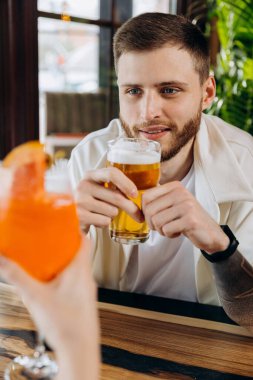 Gülümseyen çekici adam, arkadaşlarıyla barda otururken bira içiyor.