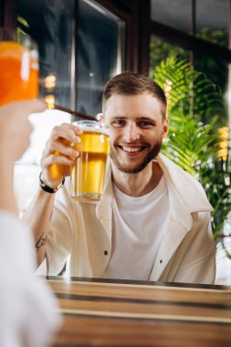Gülümseyen çekici adam, arkadaşlarıyla barda otururken bira içiyor.