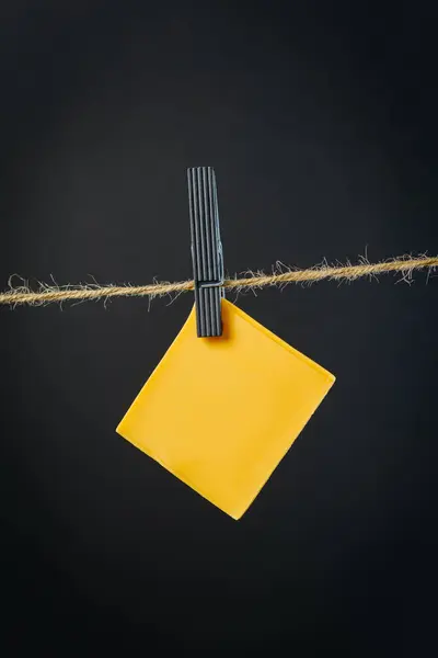 Slices of cheddar cheese hanging by a thread on dark paper background. High quality photo