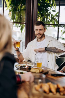 Barda ya da barda arkadaşlarıyla eğlenirken bira içen ve gülen genç adam.