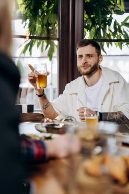 Barda ya da barda arkadaşlarıyla eğlenirken bira içen ve gülen genç adam.