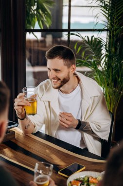 Barda ya da barda arkadaşlarıyla eğlenirken bira içen ve gülen genç adam.