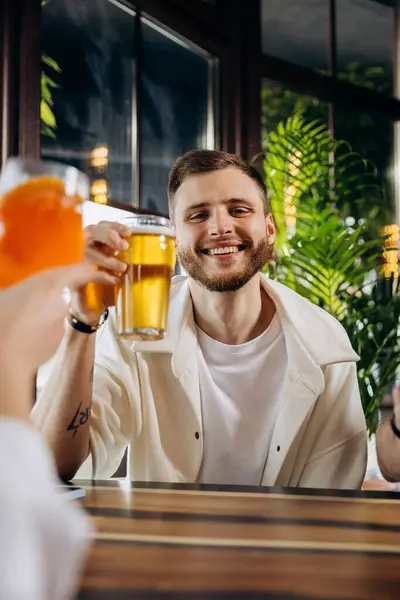 Smiling man is drinking beer while sitting at in pub with friends company