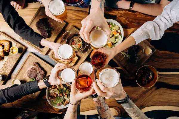 Friends cheering beer glasses on wooden table with food. Food and beverage lifestyle concept