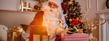 Noel ağacının yanında parlayan hediyesiyle sürpriz Noel Baba. Reklam pankartı