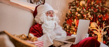 Noel Baba evde oturuyor ve dizüstü bilgisayarında yeni yıl dilek listesi ile e-posta okuyor.