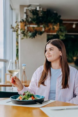 Gülümseyen kadın lezzetli yemekler yiyor ve restoranda şarap içiyor.