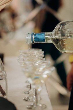 Garson düğün resepsiyonundaki masada kristal bardaklarla martini dolduruyor.