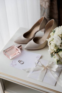 Brides wedding essentials: heels, bouquet, rings, perfume, and invitation on a white table, elegant preparation. High quality photo clipart