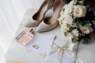 Gelinlerin düğün gereksinimleri: Topuklar, buket, yüzükler, parfüm ve davetiye beyaz bir masada, zarif bir hazırlık. Yüksek kalite fotoğraf