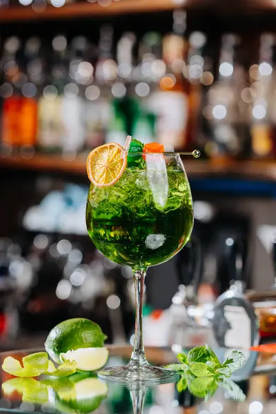 stock image Close-up of a vibrant green cocktail with orange garnish and colorful skewer in a glass full of ice