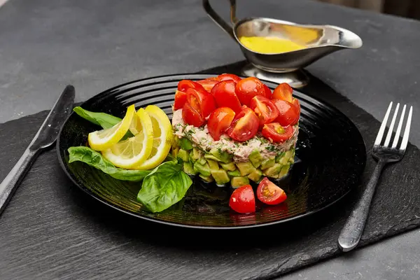 stock image Fresh avocado and tuna salad topped with cherry tomatoes, garnished with lemon slices and basil. High quality photo