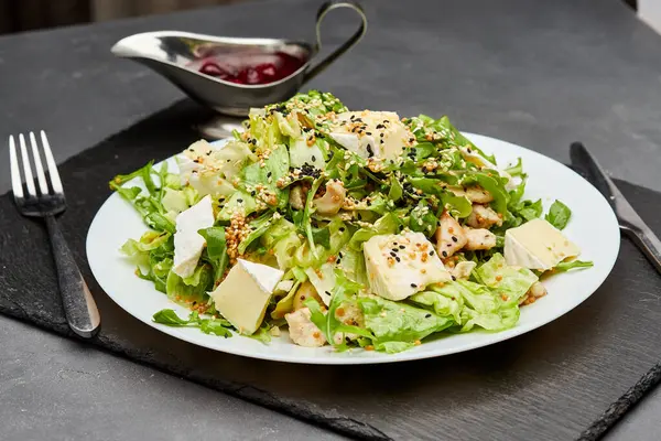 stock image Fresh green salad with chicken, brie cheese, and sesame seeds, served with berry sauce on the side. High quality photo