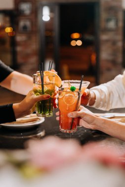 Bir grup arkadaş canlı bir bar ortamında kokteyllerle kadeh kaldırıyor, birlikteliğimizi kutluyorlar.