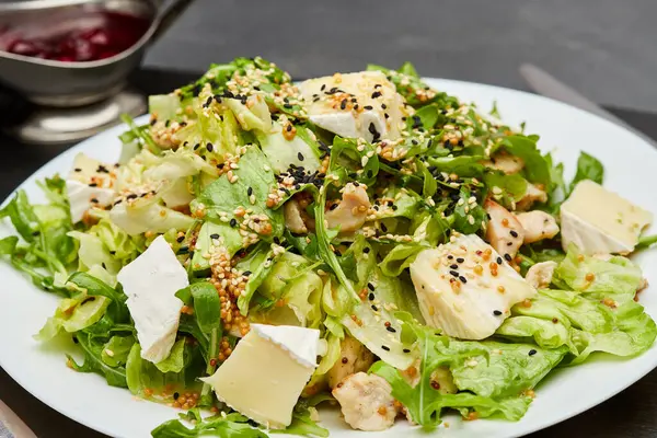 stock image Fresh green salad with chicken, brie cheese, and sesame seeds, served with berry sauce on the side. High quality photo