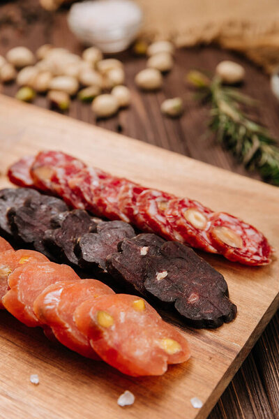 Sliced sausage with pistachios on wooden board, ideal for food presentations and gourmet displays. High quality photo