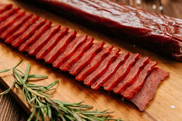 stock image Sliced gourmet smoked salami on a wooden board with herbs, perfect for charcuterie boards and snacks. High quality photo