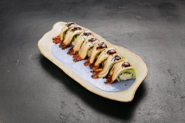 Lezzetli sosla kaplanmış kremalı yılan balığı suşi rulosu ve şık bir tabakta susam tohumları. Yüksek kalite fotoğraf