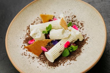 Beyaz çikolatalı gurme tatlı, bisküvi parçaları, nane ve dokulu bir tabakta yenilebilir çiçekler. Yüksek kalite fotoğraf