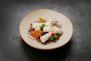 Beyaz çikolatalı gurme tatlı, bisküvi parçaları, nane ve dokulu bir tabakta yenilebilir çiçekler. Yüksek kalite fotoğraf