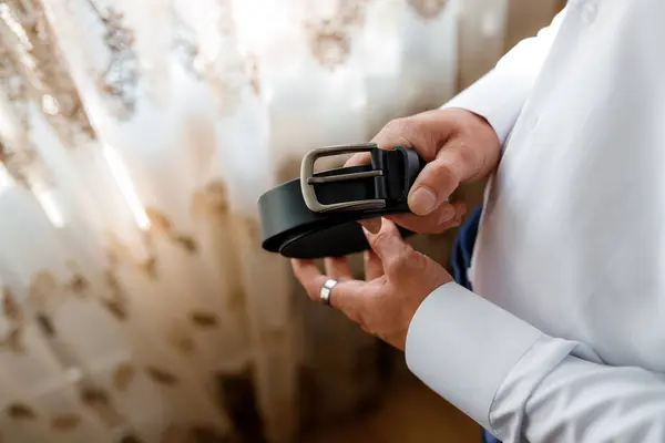 stock image Man preparing for an event holding a black leather belt, showing elegant and sophisticated style. High quality photo