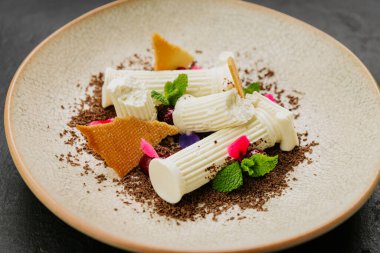 Beyaz çikolatalı gurme tatlı, bisküvi parçaları, nane ve dokulu bir tabakta yenilebilir çiçekler. Yüksek kalite fotoğraf