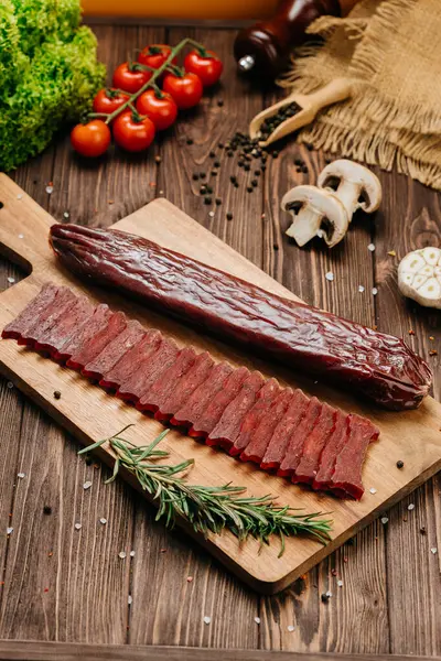 stock image Sliced gourmet smoked salami on a wooden board with herbs, perfect for charcuterie boards and snacks. High quality photo