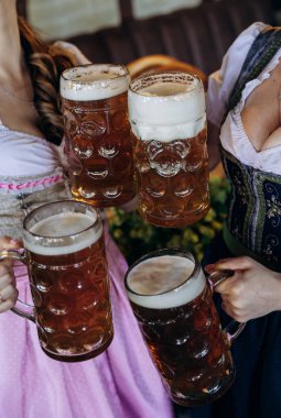 Women in traditional dirndl dresses toasting with beer mugs at Oktoberfest, German festival . High quality photo clipart