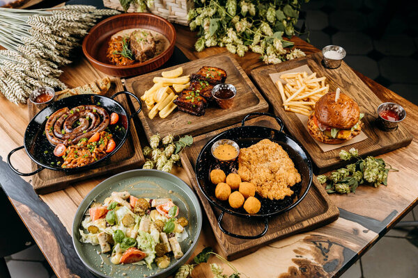 Top view of gourmet food dishes including sausages, ribs, schnitzel, salad, and burger on table. High quality photo