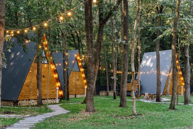 Orman ortamında parlayan sicim ışıkları olan modern A-frame kamaraları, barışçıl bir geri çekilme için ideal. Yüksek kalite fotoğraf