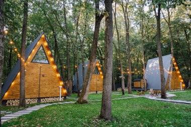 Orman ortamında parlayan sicim ışıkları olan modern A-frame kamaraları, barışçıl bir geri çekilme için ideal. Yüksek kalite fotoğraf
