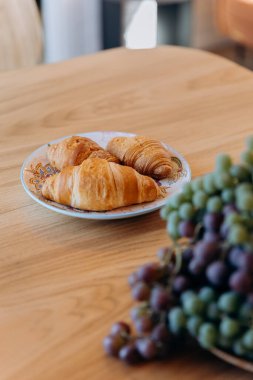 Fresh croissants on a plate, served with grapes on a wooden table for a perfect breakfast. High quality photo clipart