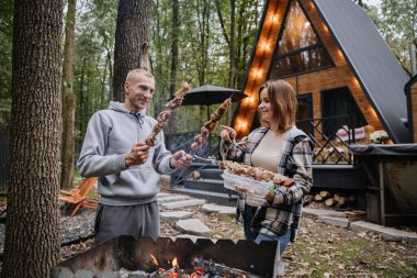 Kulübede açık ateşte barbekü için şiş hazırlayan çift, sonbahar ızgarasının keyfini çıkarıyorlar. Yüksek kalite fotoğraf