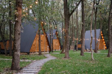 Orman ortamında parlayan sicim ışıkları olan modern A-frame kamaraları, barışçıl bir geri çekilme için ideal. Yüksek kalite fotoğraf