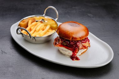 Gevrek pastırmalı gurme burger, ahududu sosu ve hoşgörülü bir yemek deneyimi için patates kızartması. Yüksek kalite fotoğraf