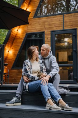 Sevgi dolu bir çift kedileriyle birlikte ahşap kulübenin merdivenlerinde oturmuş, doğada sıcak bir anın tadını çıkarıyorlar. Yüksek kalite fotoğraf
