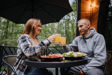 Dışarıda yemek ve bira içen, kahkaha atan ve orman terasında iletişim kuran bir çift. Yüksek kalite fotoğraf