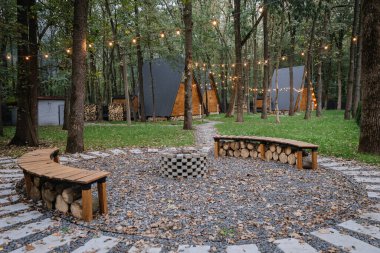 Ormandaki sıcak ateş çukuru oturma yerinde parlak ip ışıkları ve modern ahşap kulübeler var. Yüksek kalite fotoğraf