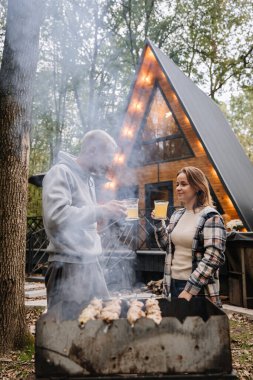 Barbekü ve doğa inzivasının tadını çıkaran, açık havada ızgaranın yanında bira içen çift. Yüksek kalite fotoğraf