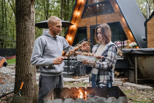 Kulübede açık ateşte barbekü için şiş hazırlayan çift, sonbahar ızgarasının keyfini çıkarıyorlar. Yüksek kalite fotoğraf