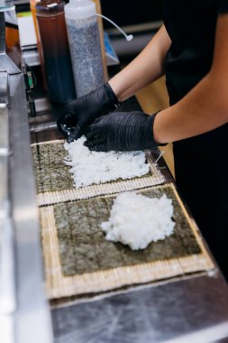 Şef özenle suşi hazırlıyor, lezzetli el yapımı rulo için Norveç çarşaflarına pirinç seriyor. Yüksek kalite fotoğraf