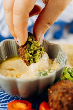 Dipping a crunchy falafel in creamy hummus for a delicious, plant based Mediterranean snack. High quality photo clipart