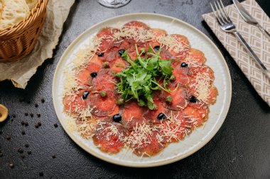 Kırmızı şarap ve taze ekmekle servis edilen roka, parmesan, kapari ve zeytinli sığır eti carpaccio. Yüksek kalite fotoğraf