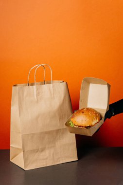 Burger takeaway concept with eco-friendly packaging on vibrant orange background. High quality photo clipart