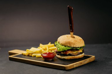 Klasik hamburger, taze marul ve domates yanında kızarmış patates ve ketçapla ahşap bir tahtanın üzerinde servis edilir. Yüksek kalite fotoğraf