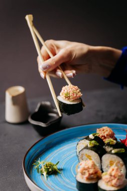 Soya soslu mavi bir tabakta servis edilen yengeç soslu suşi rulosunu tutmak için çubuk kullanmak. Yüksek kalite fotoğraf